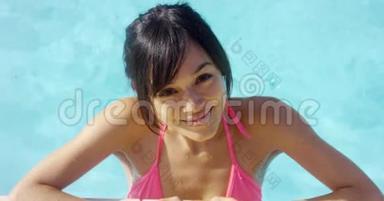 穿着粉色比基尼的浅黑色的微笑女郎站在泳池边