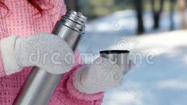 女人从金属热水瓶里倒热饮料，手戴针织手套把茶倒进杯子里，手拿热水瓶