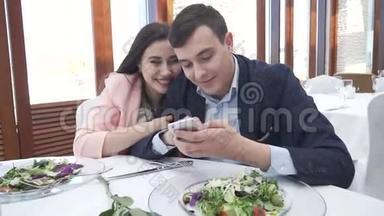 一对恋爱中的情侣在餐馆里浏览社交网络上的iPhone股票视频