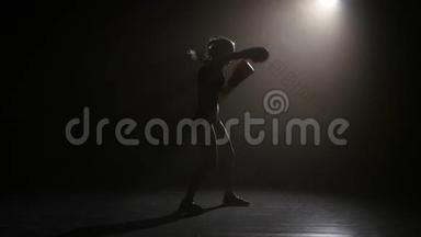 拳王拳击手发出拳打脚踢。 剪影。 后方有灯光。 黑色背景。 侧视图