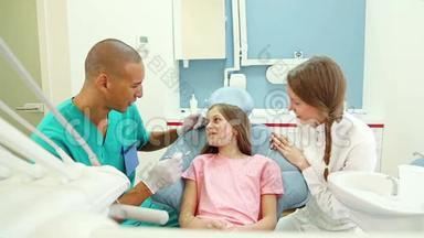 微笑的年轻女孩与牙医和助手交谈，显示她<strong>疼痛</strong>的<strong>牙齿</strong>
