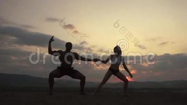 在山顶日落时做体操运动的运动型肌肉男教练的剪影