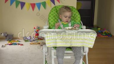 幼儿男孩坐在婴儿高喂养的椅子上<strong>用勺子</strong>吃土豆泥