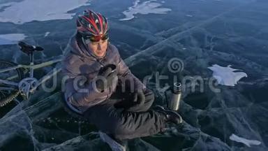 那个人正坐在冰上自行车的轮子上休息。 他<strong>喝热水</strong>瓶里的茶。 骑自行车的人穿着
