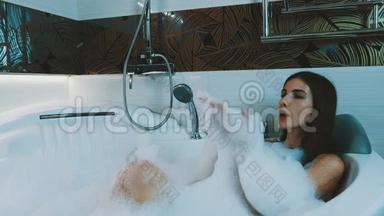 快乐的女孩在浴室里洗了满是泡沫的澡。 好好享受。 在肥皂泡沫上吹气。