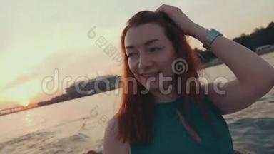 年轻的红发女孩穿着绿松石的裙子坐在帆船上。 日落。 舞蹈