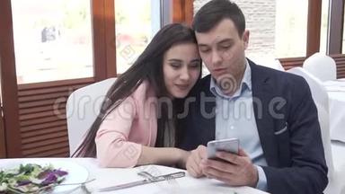一对恋爱中的情侣在餐馆里浏览社交网络上的iPhone股票视频