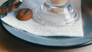 女人正在咖啡馆里端着一个茶碟和一个拿铁玻璃杯，茶碟上放着一块咖啡豆形式的饼干