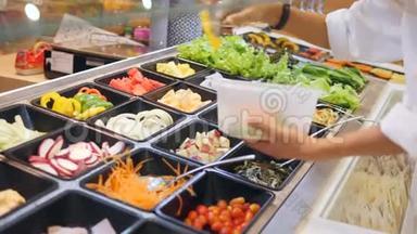 年轻的高加索女人在<strong>食品店</strong>的沙拉酒吧买有机蔬菜。 素食者带走食物健康饮食