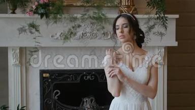 美丽活泼的黑发新娘，穿着白色连衣裙，摆在壁炉背景上