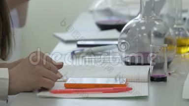 在化学实验室工作的学生在笔记本上做笔记。 科学课用电话的女学生