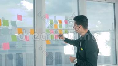 年轻的帅哥在现代办公室的全景窗口上写着粘稠的笔记。 头脑风暴，命名..