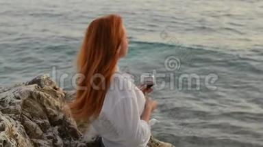 在亚得里亚海的岩石海滩上，一个头发飞扬的年轻女子站着一杯酒