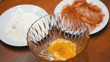在家庭厨房里的面粉和肉的背景下，碎蛋落入透明碗中。 慢动作
