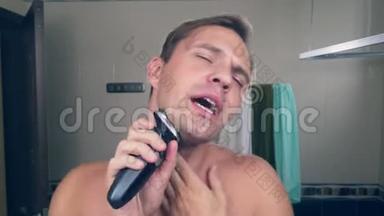 一个有趣的帅哥在浴室里用电动剃须刀刮胡子，在镜子前唱<strong>歌</strong>。 4k.