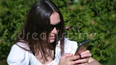 女人在阳光明媚的日子里坐在公园里，聊天，在<strong>手机</strong>上<strong>输入</strong>一条信息。