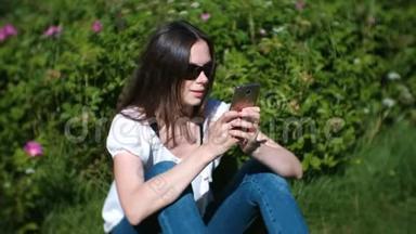 女人在阳光明媚的<strong>日</strong>子里坐在公园里，聊天，在<strong>手机</strong>上输入一条信息。