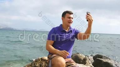 微笑的年轻人在海边用智能手机打视频电话。 快乐的男人在网上聊天视频