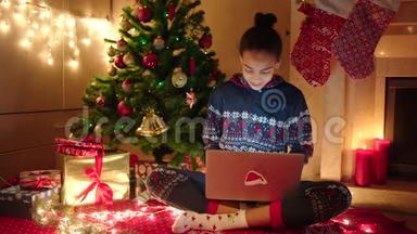 年轻的黑人妇女使用笔记本电脑上网聊天，坐在装饰好的圣诞树旁