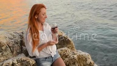 在亚得里亚海的岩石海滩上，一个<strong>头发飞扬</strong>的年轻女子站着一杯酒