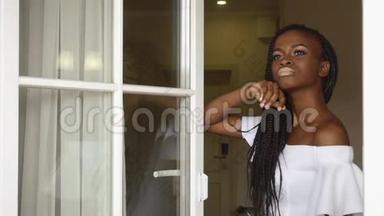 优雅的非裔美国女士体贴地透过窗户看着豪华酒店公寓的背景