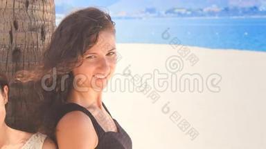 穿着黑色连衣裙的苗条女孩在手掌上说着海滩上的微笑