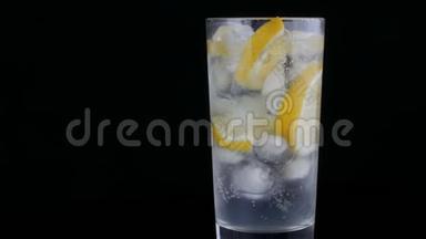 用冰块和黑色背景的冷苏打在一个长杯子里切成柠檬。 清爽柠檬泡沫。
