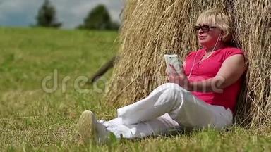 有着白色智能手机的女人坐在干草堆旁听音乐