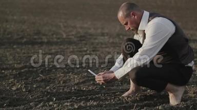 一个留胡子的人带着手机在<strong>田野</strong>里的肖像。 一个人光着脚在<strong>田野</strong>里给植物拍照。