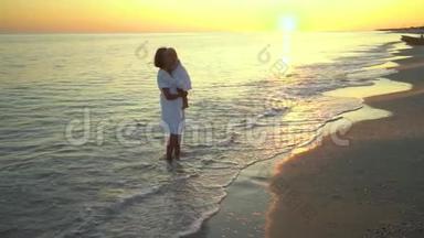 日落时分，年轻漂亮的女人和她的小女儿在海滨散步。 <strong>妈妈</strong>把女儿抱在<strong>怀里</strong>。 他们