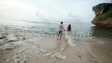 新婚夫妇在傍晚或日落时在海边散步。 牵手，拥抱。 在海洋附近浪漫。
