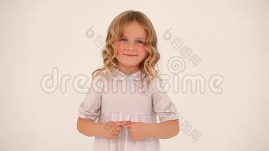 可爱的小可爱的小女孩蹒跚学步的孩子，一头金色卷发，穿着白色连衣裙，用手指在空中画出一颗大大的心。