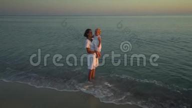日落时分，年轻漂亮的女人和她的小女儿在海滨散步。 <strong>妈妈</strong>把女儿抱在<strong>怀里</strong>。 他们