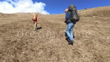 两个戴着帽子和太阳镜背包的游客摄影师带着相机在黄草上山