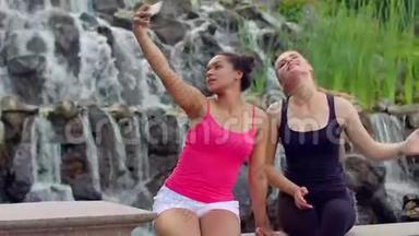 自私的女人。 两个年轻女人在瀑布附近自拍。 女人自拍