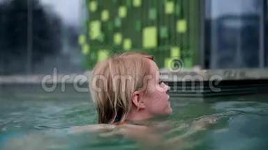 穿着蓝色比基尼的年轻女人<strong>远离</strong>相机，在户外游泳池里尽情享受。