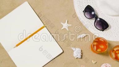 沙滩沙上的笔记本、鸡尾酒、帽子和墨镜