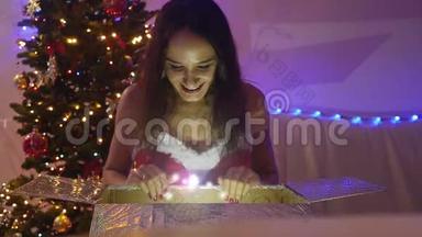 年轻快乐的美丽女子坐在<strong>神</strong>奇的圣诞礼物和圣诞树前，慢慢地<strong>看</strong>着闪闪发光的<strong>灯</strong>光