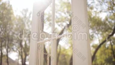 白色的拱门和带垫子的椅子。 婚礼拱门以乡村风格的门的形式。 太阳透过阳光照耀