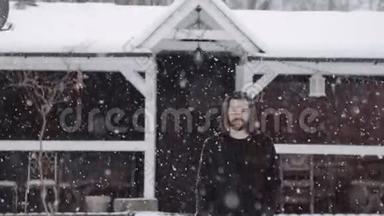 穿着黑色毛衣的英俊男子走在大雪纷飞的旧木<strong>屋前</strong>。