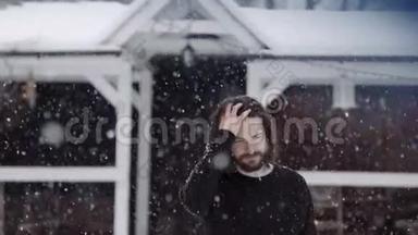 穿着黑色毛衣的英俊男子走在大雪纷飞的旧木屋前。