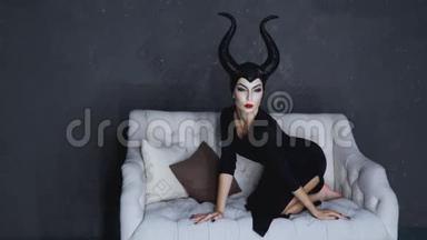 一个长着黑色大角的漂亮女孩描绘了一个女巫Maleficent，并在一张白色<strong>沙发上</strong>为<strong>摄影</strong>师摆姿势