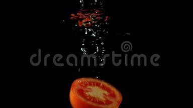 一半的红番茄落在水下超慢动作镜头下。 黑色背景