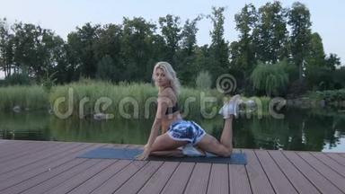 日落时分，一个金发的运动女孩正<strong>忙着</strong>在池塘边伸展