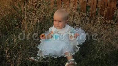 一个<strong>小女孩</strong>坐在高高的<strong>草地上</strong>，穿着白色的裙子，吃着杏子。 夏天日落。