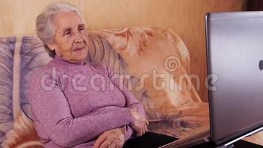 坐在沙发上用<strong>笔记本</strong>电脑打字的老年妇女。 金属<strong>笔记本</strong>电脑。