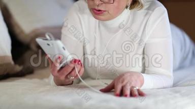 带着白色智能手机的老妇人躺在床上