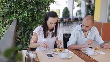 年轻夫妇在户外咖啡馆的一张桌子上吃早餐和聊天