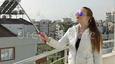 年轻快乐的女人用智能手机手机摄像头在屋顶上拍摄自我画像