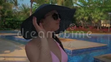 戴着蓝帽子的漂亮女孩在游泳池边散步。 夏日的阳光。 慢动作
